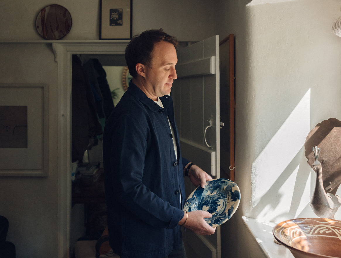 Curator Tobias Vernon holding a ceramic plate in his cottage in Wells
